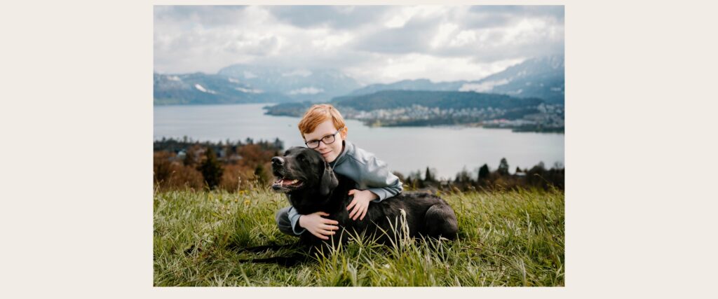 Young boy hugging a black dog above Lake Lucerne during a natural family photography session in Switzerland