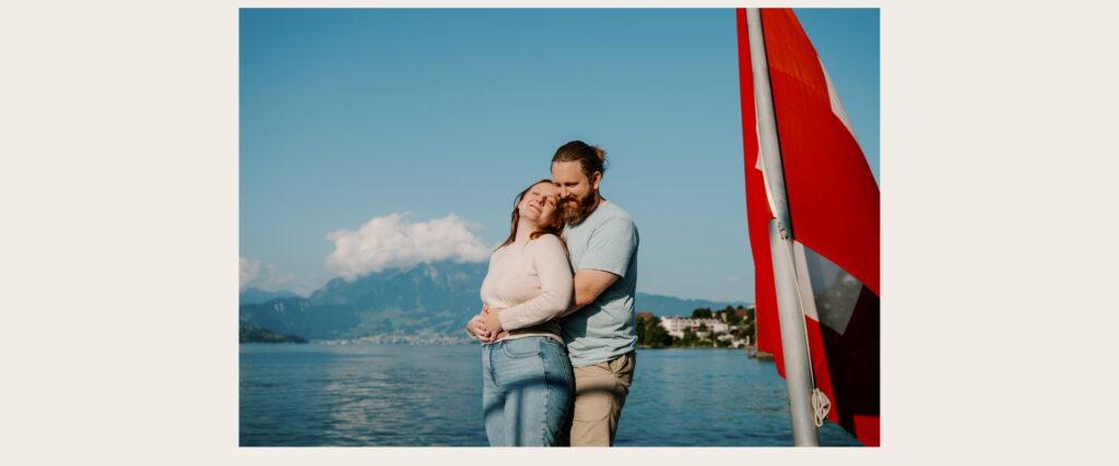 Couple embracing during a summer photography session on Lake Lucerne with the Swiss flag and mountain views.