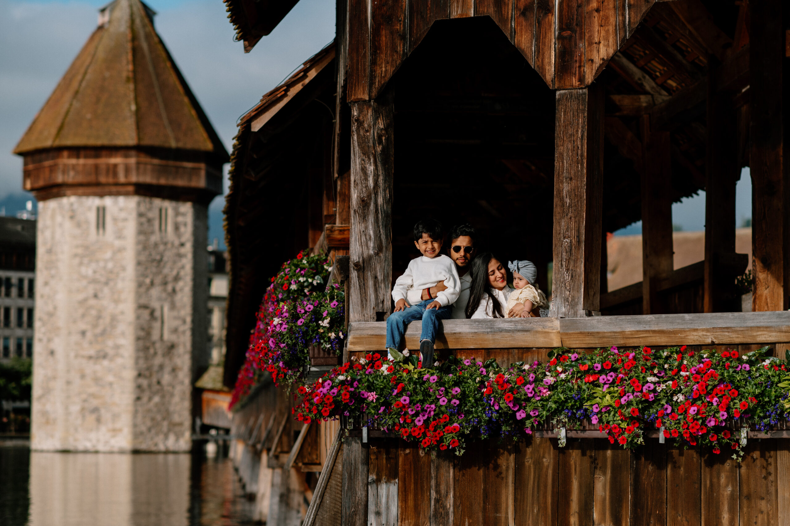 Family enjoying a morning photo session on Chapel Bridge in Luzern, Switzerland, with vibrant flowers in the foreground.