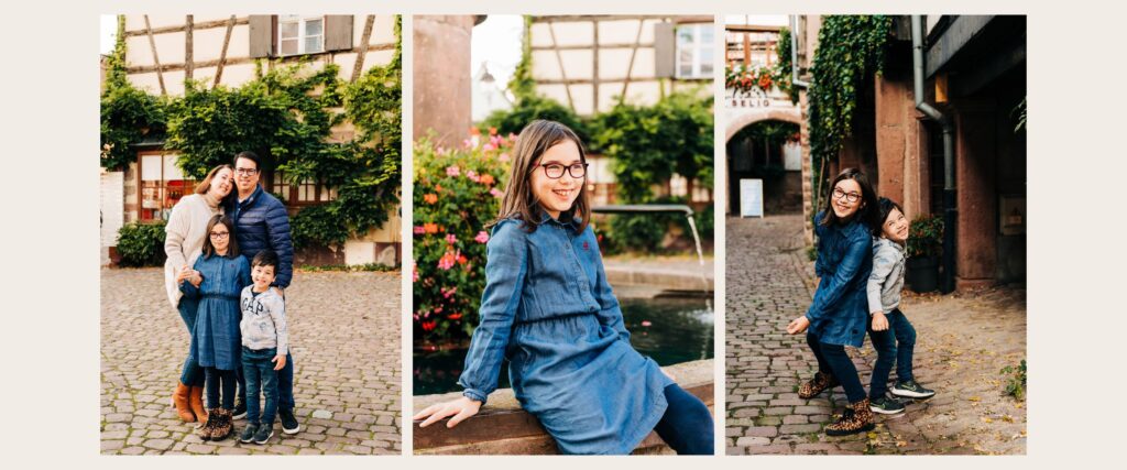 Family of four standing in Alsace village square during family photography session Young girl sitting by Alsace village fountain surrounded by flowers Girl and younger brother laughing on cobblestone street in Riquewhir